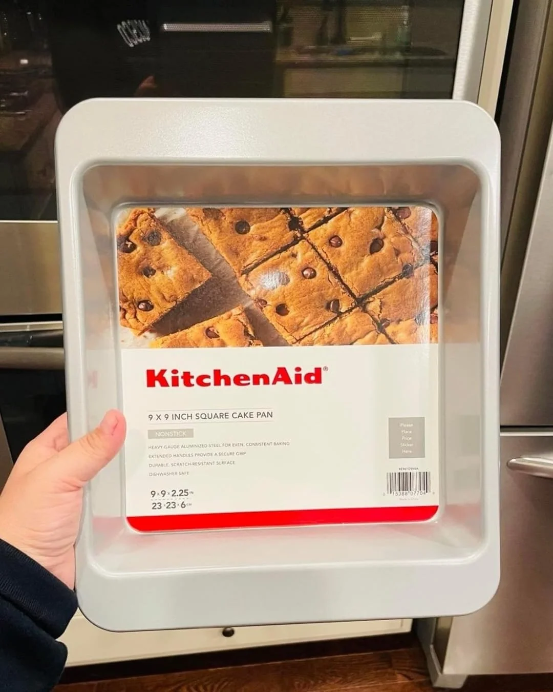 KitchenAid 9 x 9 inch square cake pan held in hand with product insert visible in kitchen