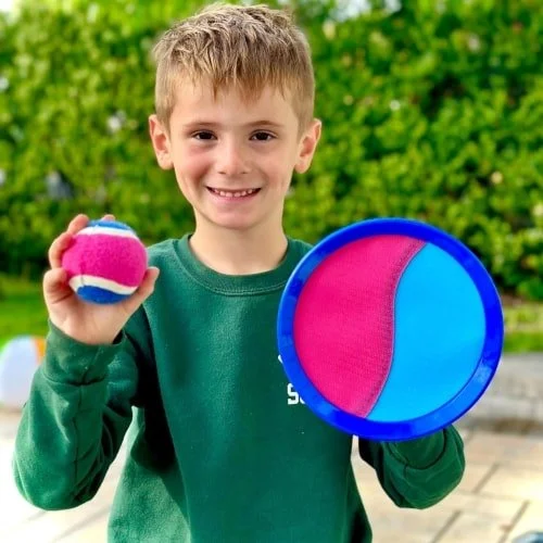 Smiling boy holding colorful ball and paddle outdoors.