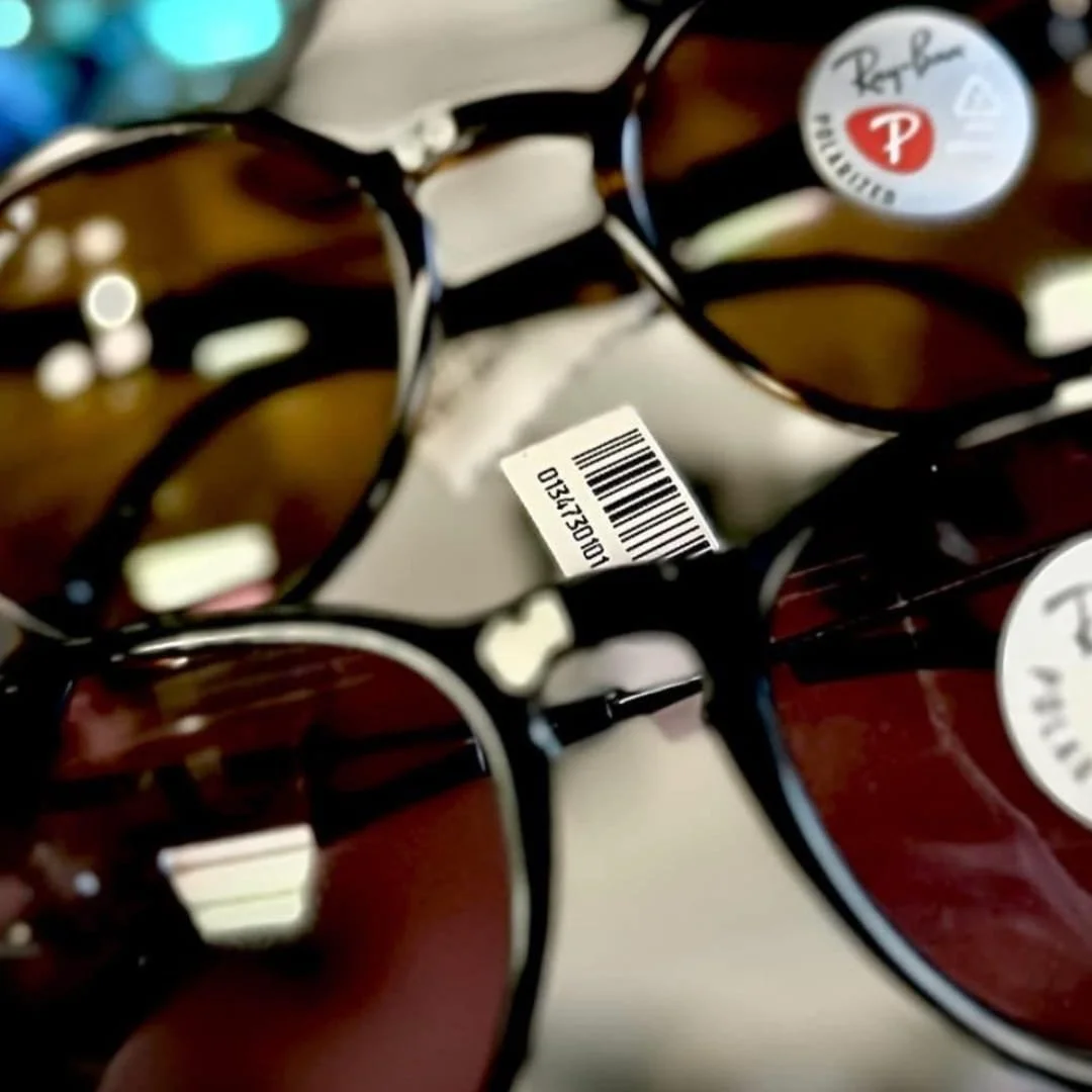 Close-up of Ray-Ban sunglasses with tortoiseshell frames and polarized dark lenses, featuring a Ray-Ban logo sticker and barcode, displayed in a retail setting.