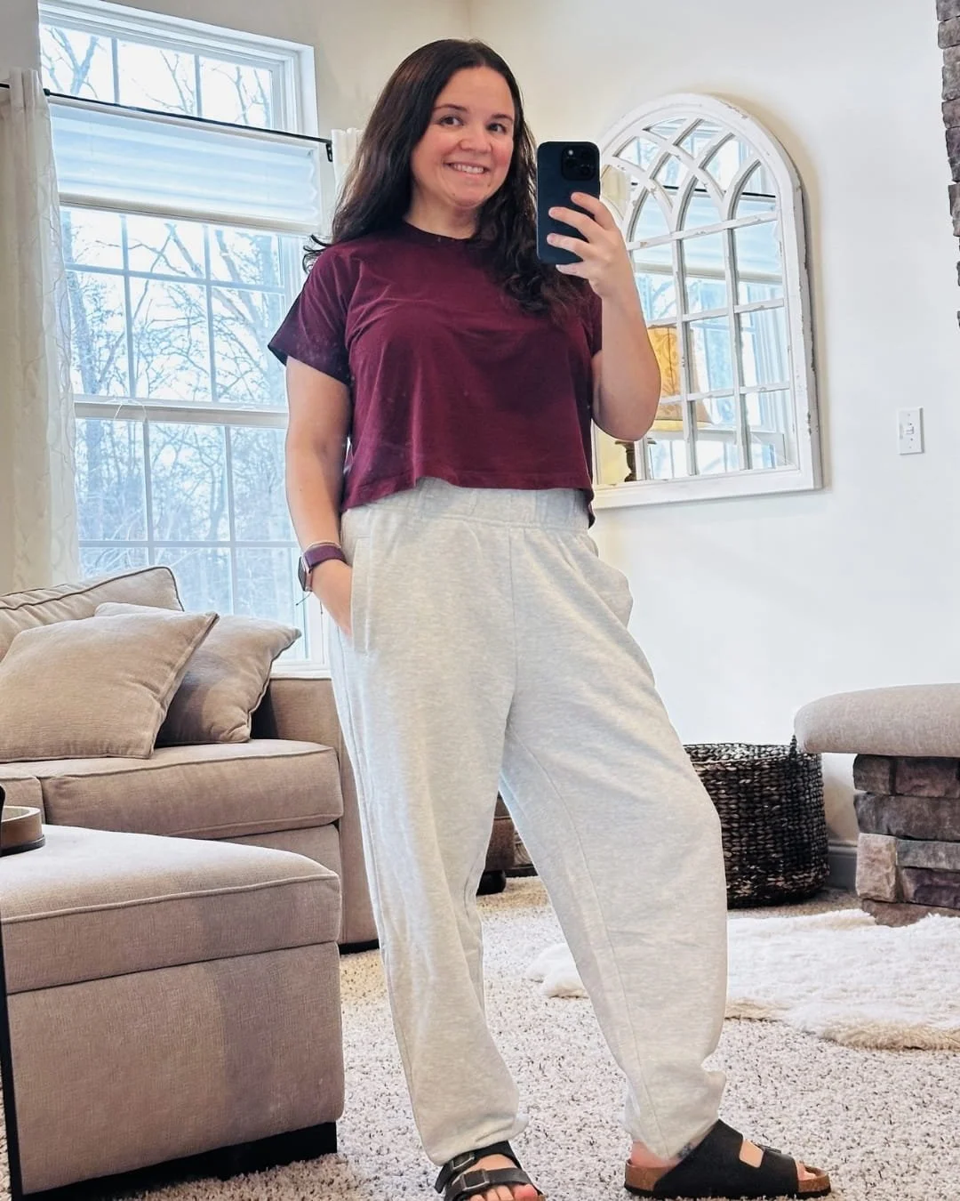 Nicole taking a mirror selfie wearing a burgundy crop top and Aerie Jet Setter Jogger sweatpants in her living room with neutral decor and soft lighting.