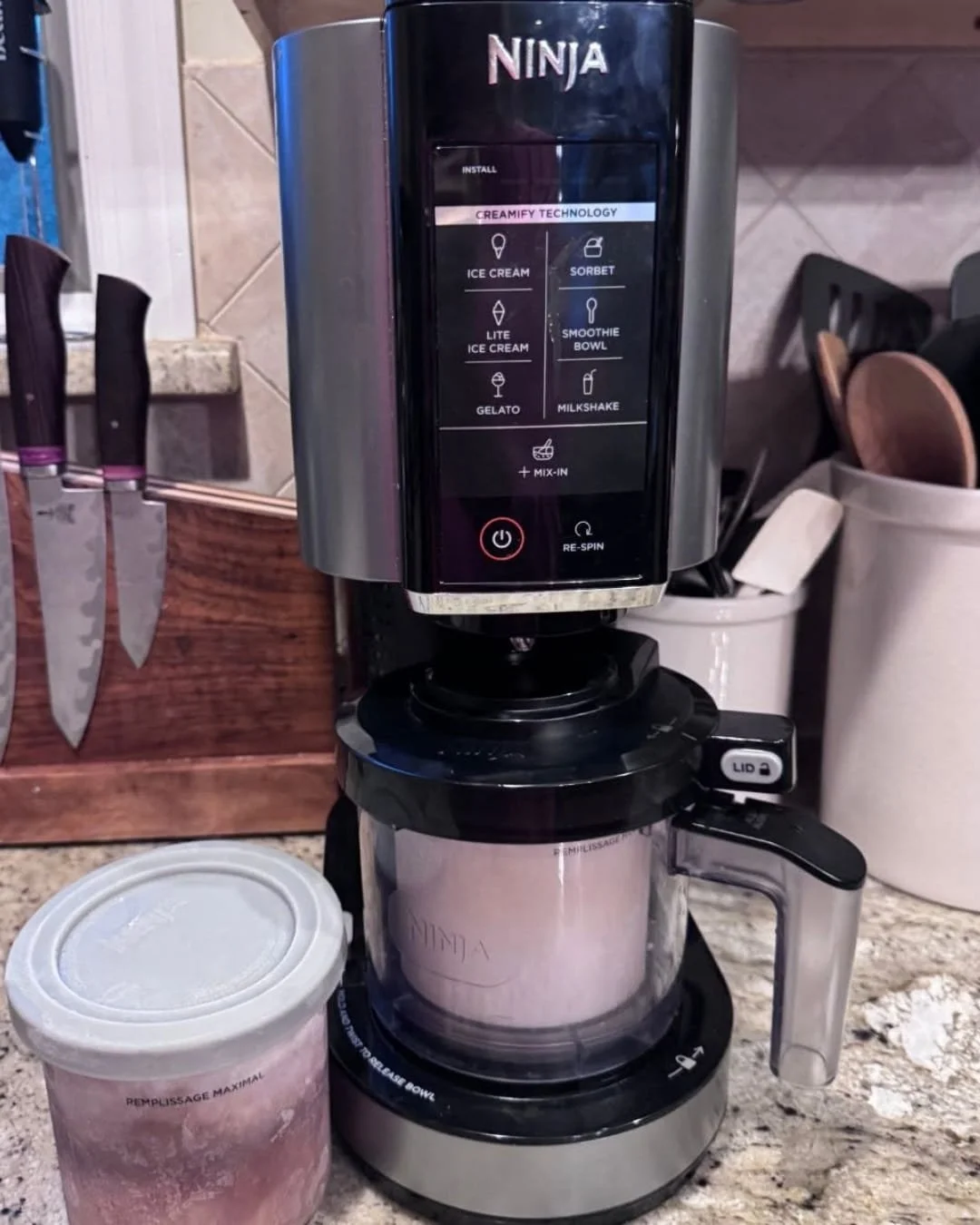 Ninja ice cream maker on a kitchen counter with a frozen pint container locked into the machine and another pint beside it