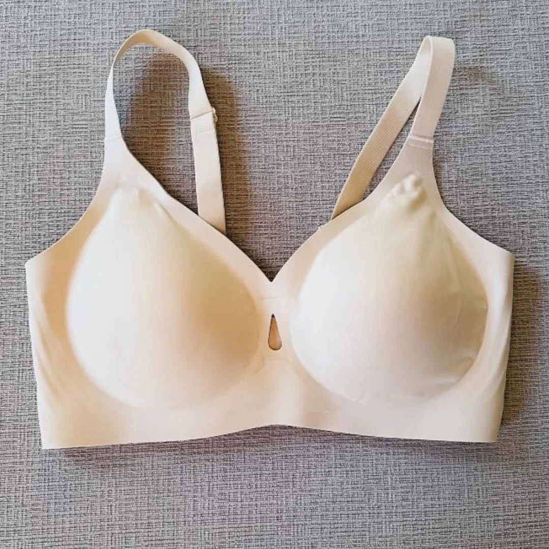 Nude LetsJoli wireless bra with smooth molded cups, adjustable straps, and a seamless wide band laid flat on a textured fabric surface