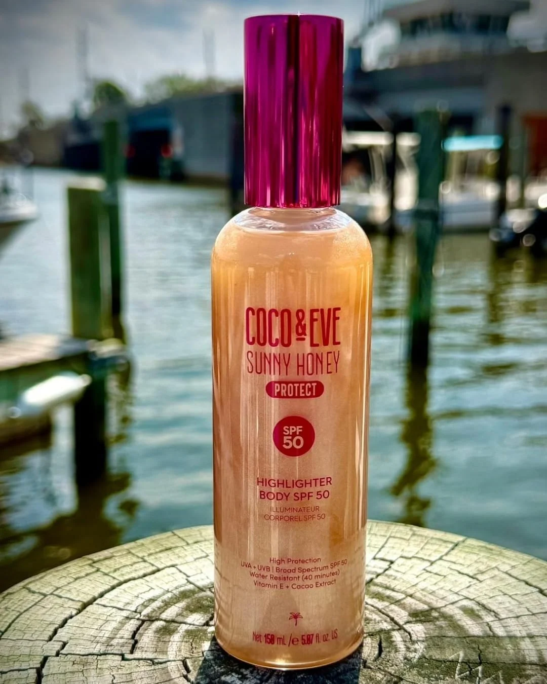 Coco & Eve shimmering body oil SPF 50 bottle displayed on a dock by the water