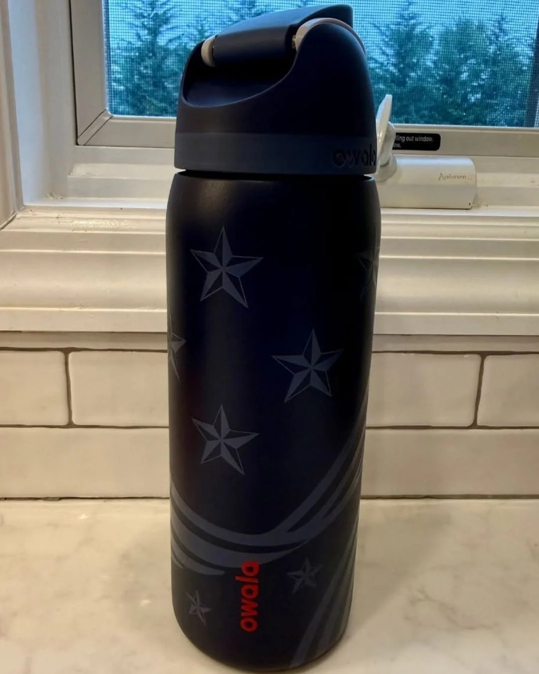 Owala FreeSip water bottle in navy blue with star pattern standing on kitchen counter