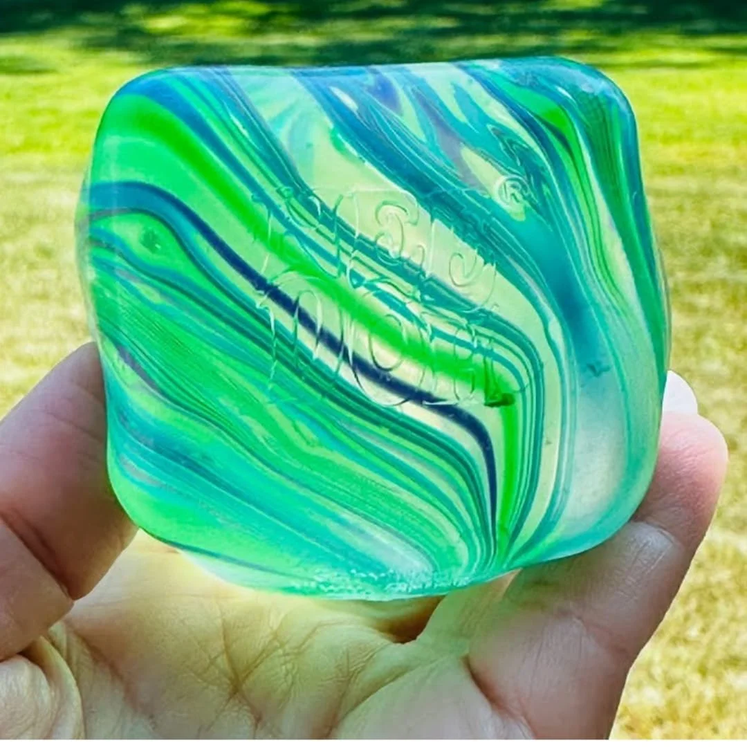 NeeDoh Nice Cube sensory toy with blue and green marbled design held outdoors in hand