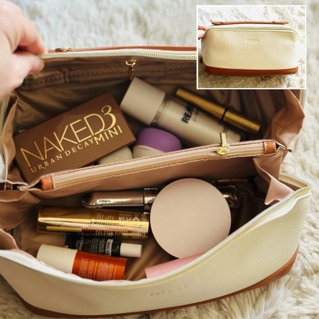 Cream-colored Telena travel makeup bag with tan trim, shown open to reveal organized compartments holding cosmetics like an Urban Decay Naked3 Mini palette, skincare bottles, and makeup tubes, resting on a white faux-fur surface.