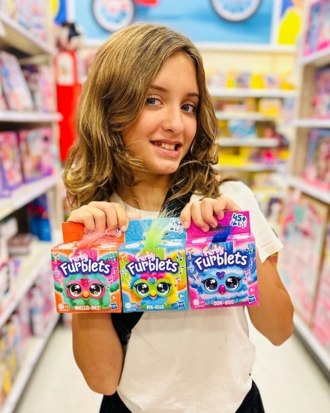 Furby Furblets Mello-Nee, Pix-Elle, and Ooh-Roo toys displayed by a child in a vibrant toy store setting.