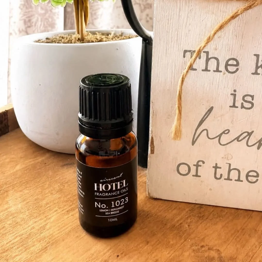 Small amber bottle of AirScent Hotel Diffuser fragrance oil displayed on a wooden surface beside rustic home decor