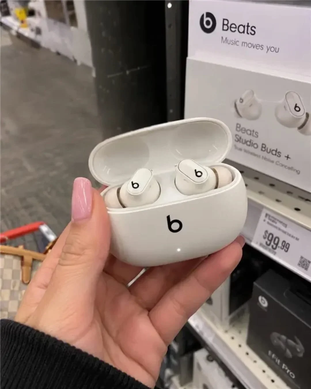 Hand holding open Beats Studio Buds charging case with wireless earbuds in front of retail store display