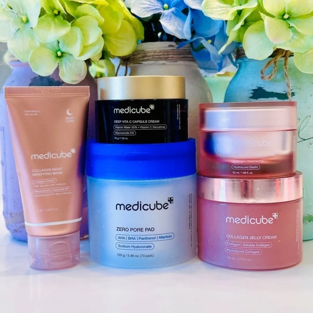 Five Medicube skincare products, including collagen creams, a Vitamin C capsule cream, and pore pads, arranged on a white surface with soft-focus hydrangeas in the background.