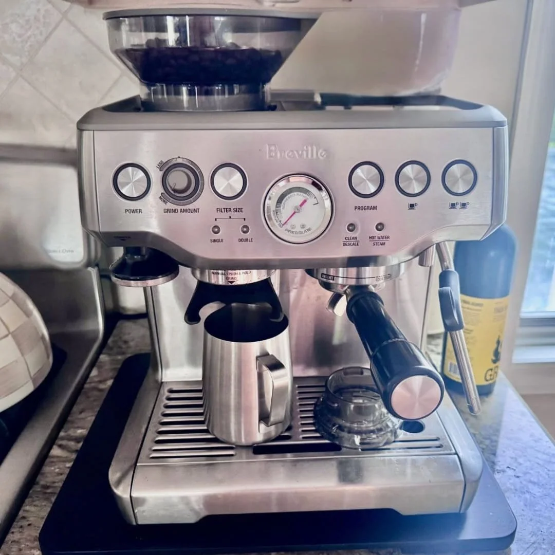 Stainless steel Breville espresso machine with built-in grinder, portafilter, and milk frothing pitcher on a kitchen counter