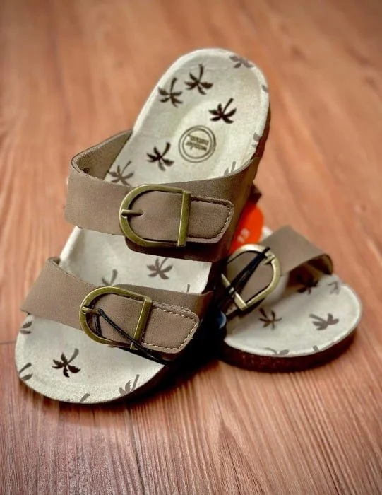 Beige sandals with buckles and patterned footbed on wooden floor.