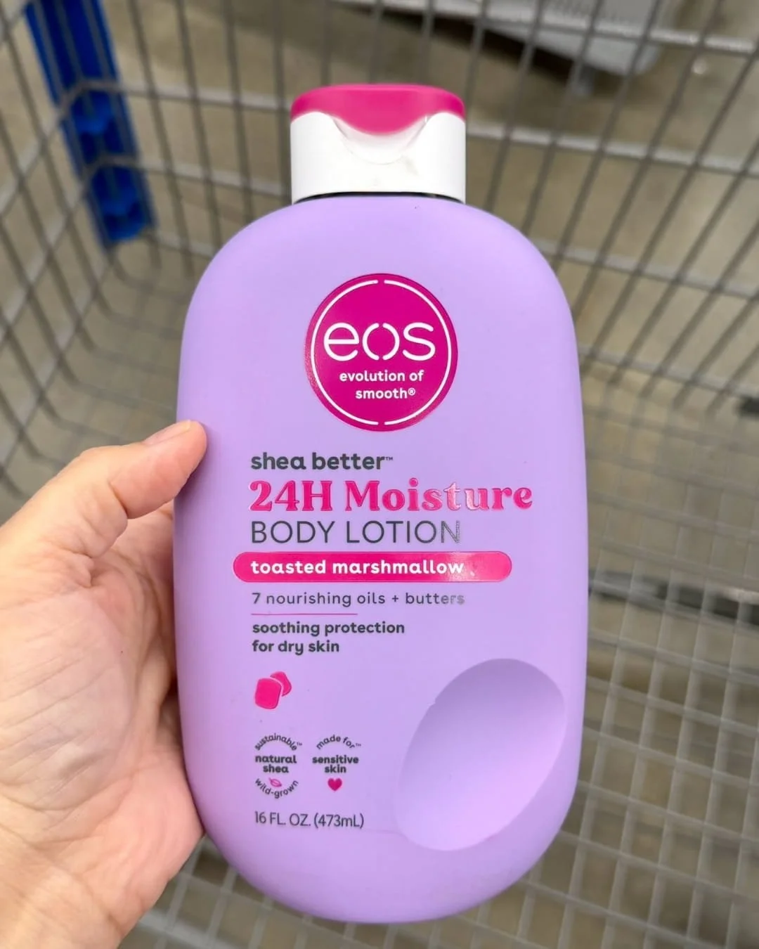 Hand holding eos Shea Better 24H Moisture Body Lotion in Toasted Marshmallow scent inside a retail store
