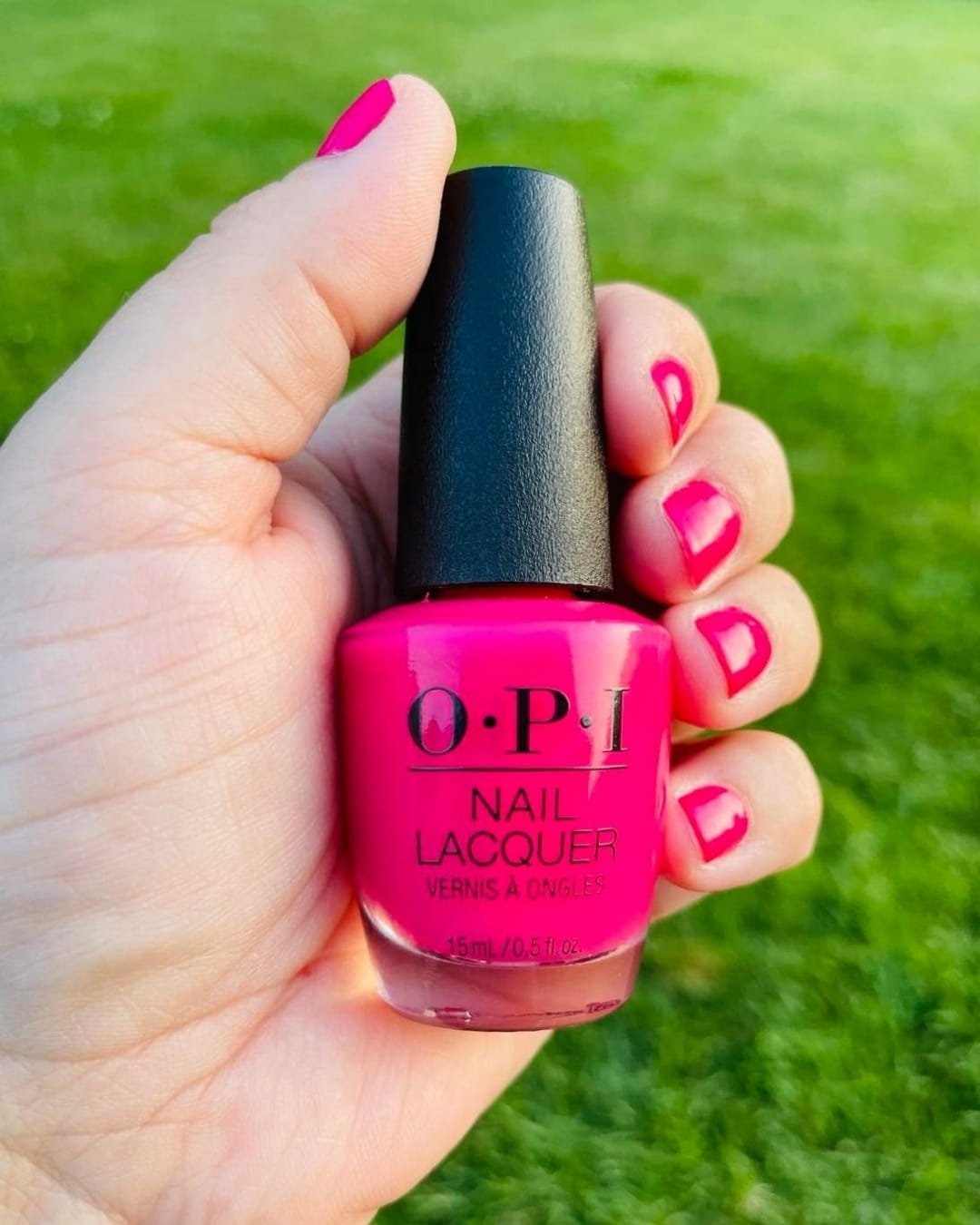 OPI hot pink nail polish bottle held in hand with matching painted nails outdoors