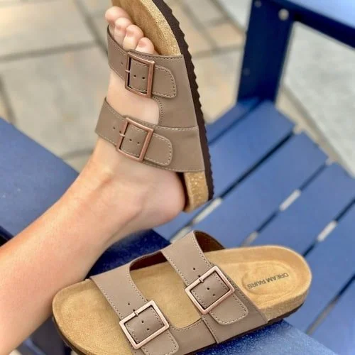Close-up of light brown DREAM PAIRS sandals with cork-like soles and bronze buckles, one worn on a foot and the other resting on a blue slatted surface.