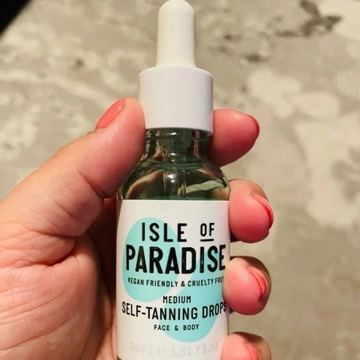 Hand holding Isle of Paradise Medium Self-Tanning Drops, vegan-friendly and cruelty-free, in a clear bottle with dropper cap.