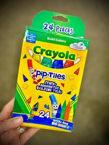 Hand holding a Crayola pip-Tiles mini-MAGNETIC BUILDING TILES box with 24 colorful pieces, featuring playful crayon characters, bold colors, and travel-friendly design.