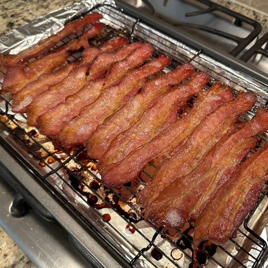 Freshly baked bacon strips on a wire rack, with rendered fat pooling on the foil-lined tray beneath.
