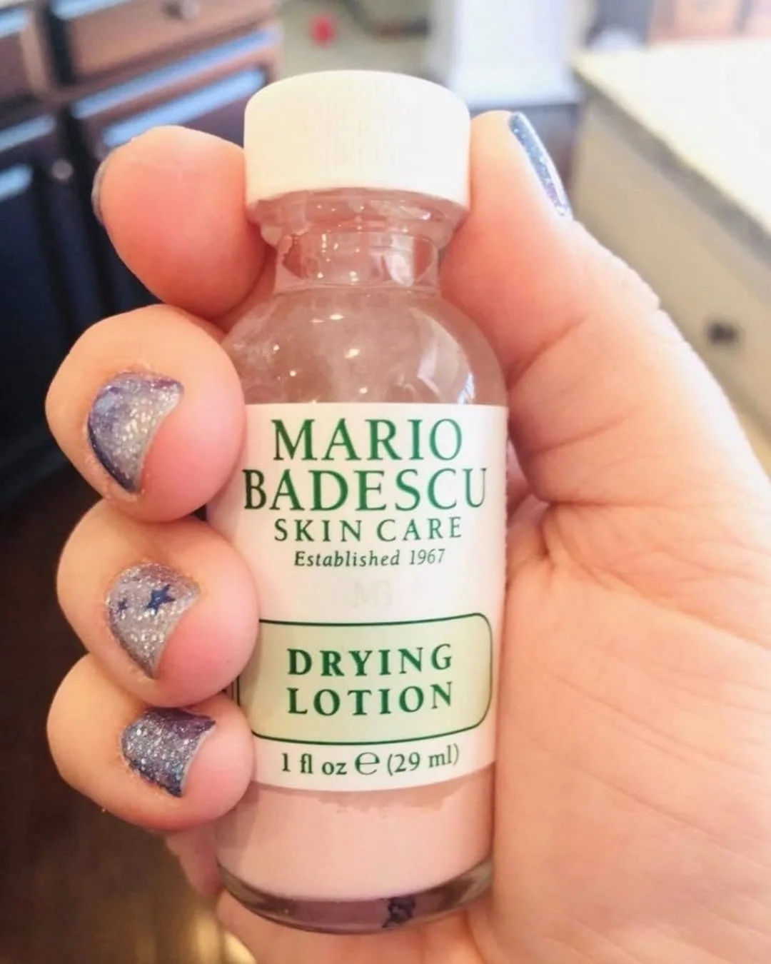 Mario Badescu Drying Lotion acne treatment bottle held in hand with pink sediment visible