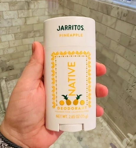 Native deodorant in Jarritos Pineapple scent, featuring bright orange-yellow and green label with pineapple graphics, held by a hand against a tiled background.