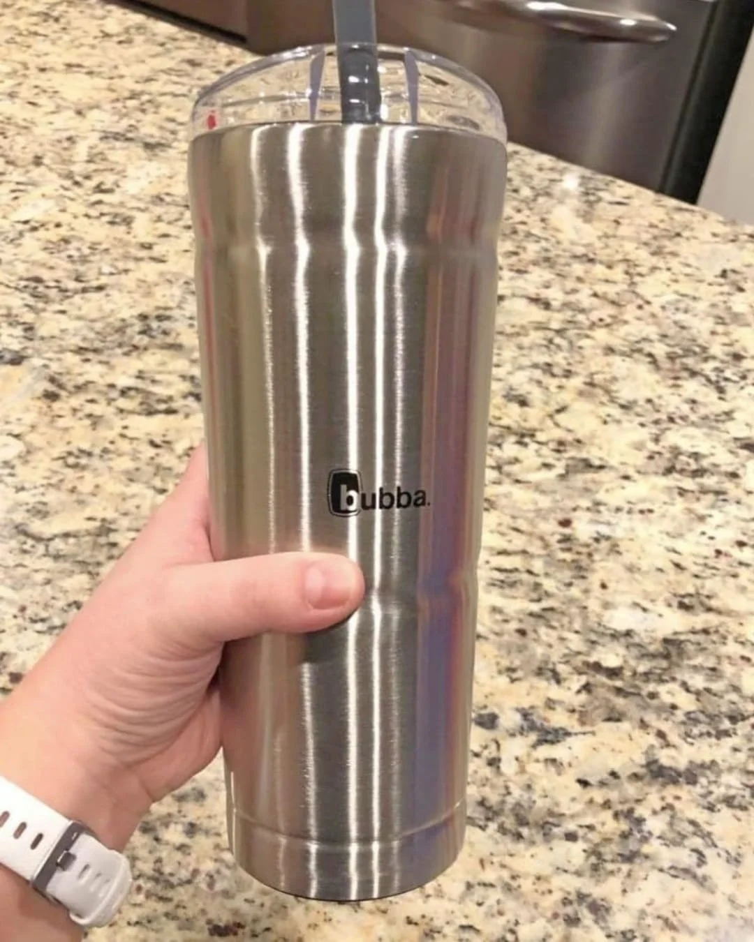 Bubba stainless steel tumbler with clear lid and black straw held in hand in kitchen