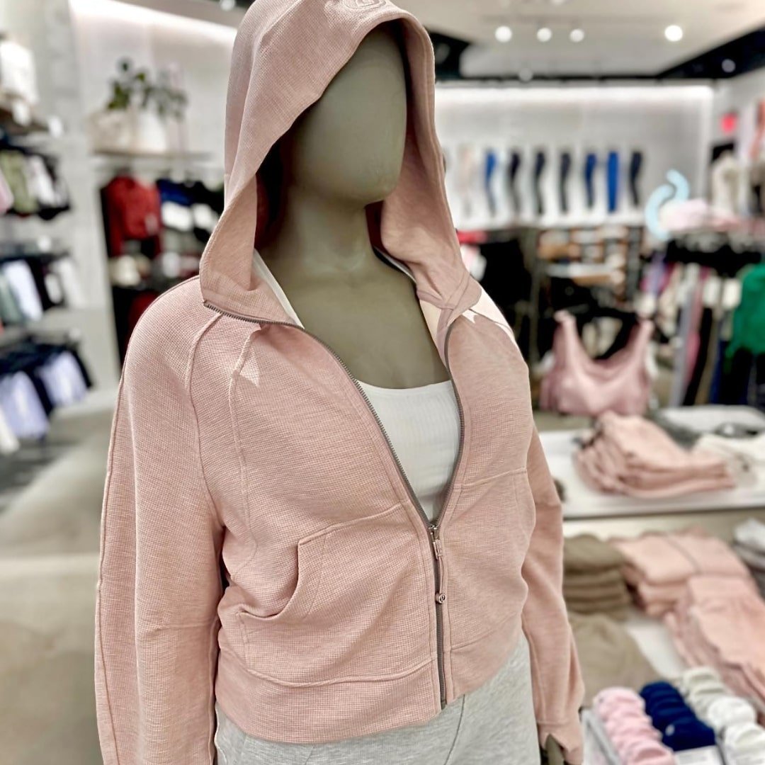 Lululemon half-zip hoodie in light pink with a textured design, displayed on a mannequin wearing a white tank top and grey athletic pants in a retail store setting.