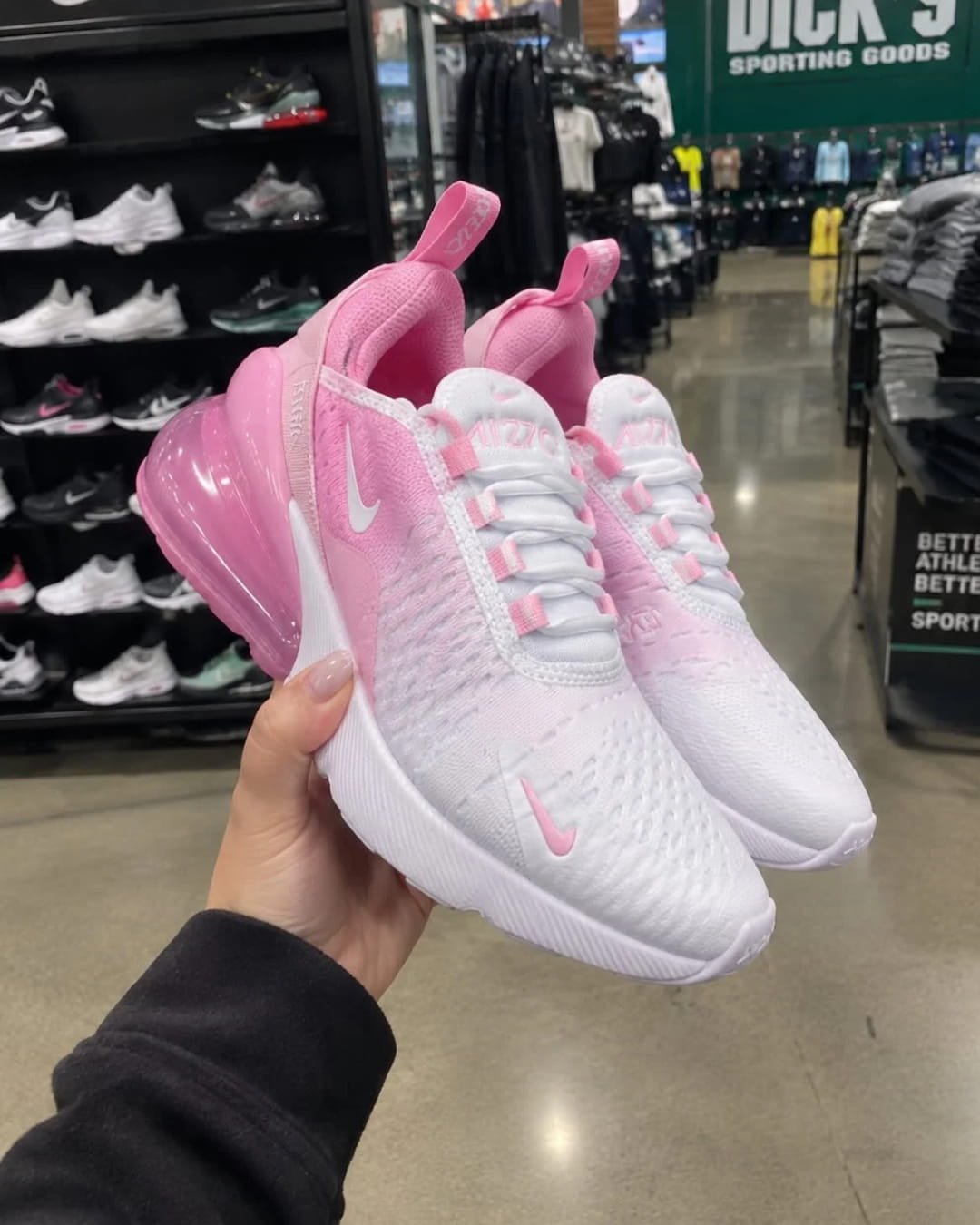 Hand holding pink and white Nike Air Max 270 sneakers inside a sporting goods store