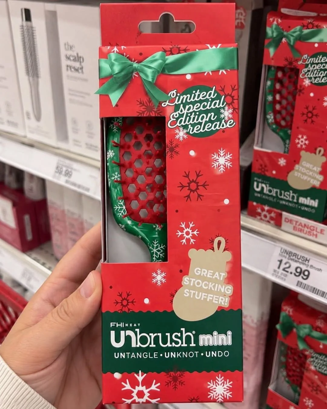 Hand holding a mini detangling hair brush in festive holiday packaging on a retail store shelf