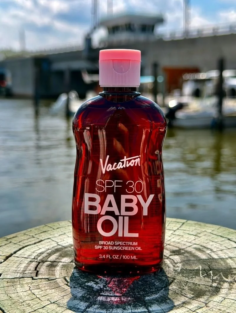 Vacation SPF 30 Baby Oil sunscreen bottle on a weathered dock post by the water