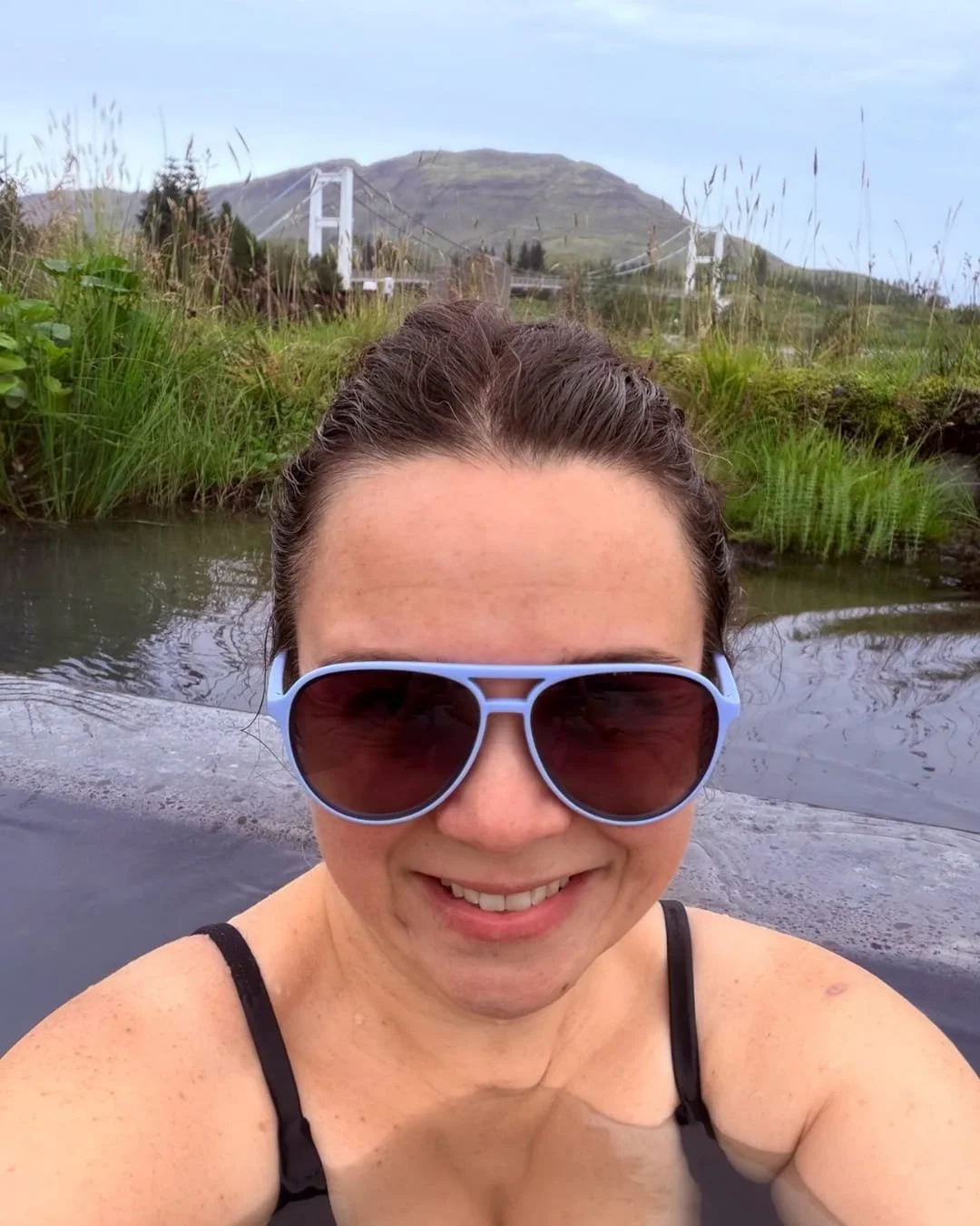 Nicole wearing blue goodr polarized sunglasses while relaxing in a hot spring outdoors
