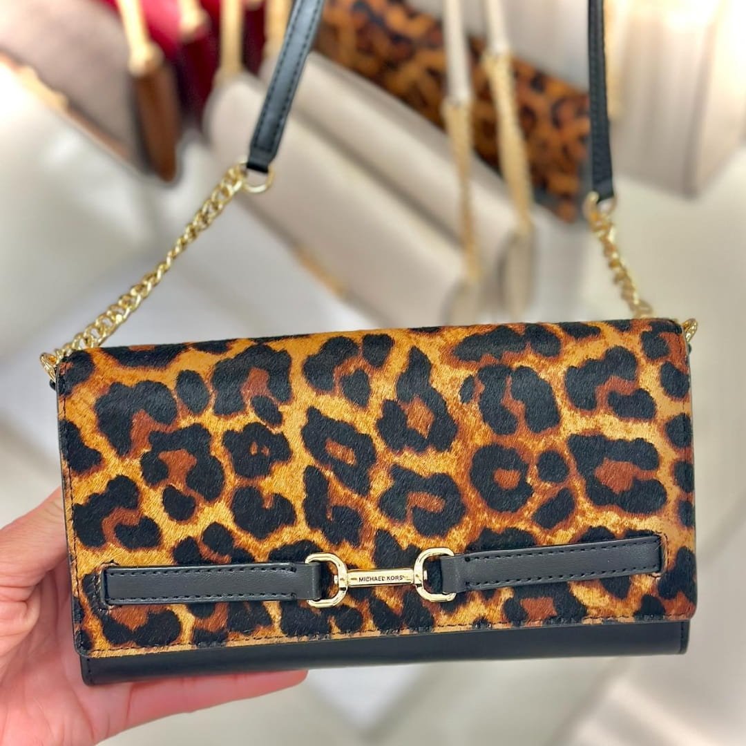 Michael Kors leopard print crossbody bag with gold chain strap, black leather accents, and gold hardware, displayed in a retail setting.