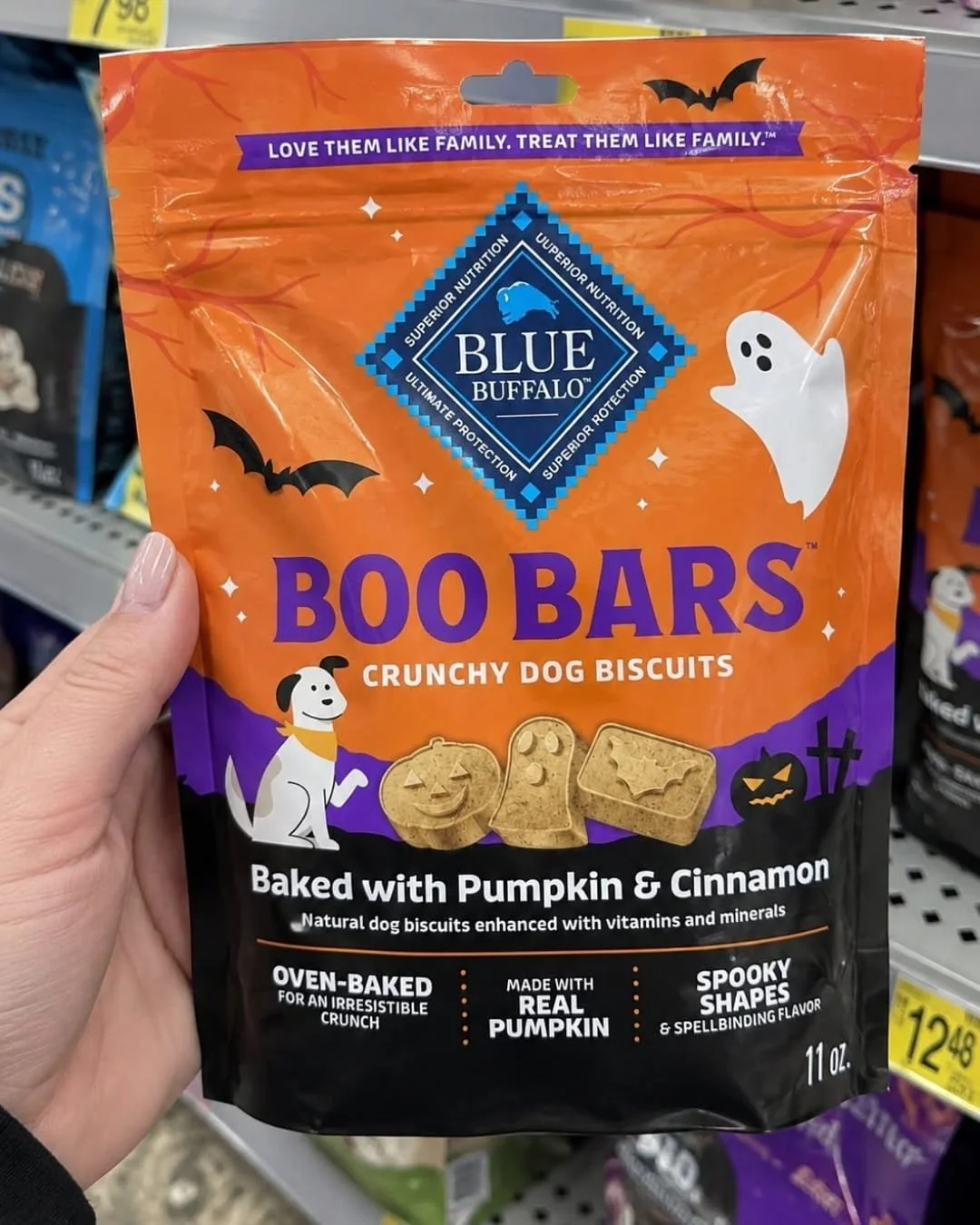 Hand holding a Blue Buffalo Boo Bars crunchy dog biscuits bag with Halloween-themed pumpkin and ghost graphics in a store