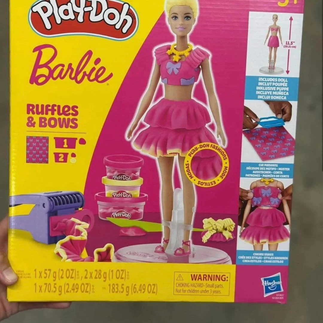 Play-Doh Barbie Ruffles & Bows set featuring a Barbie doll with customizable Play-Doh outfits, including ruffled skirts and bow designs, with tools and colorful Play-Doh tubs.