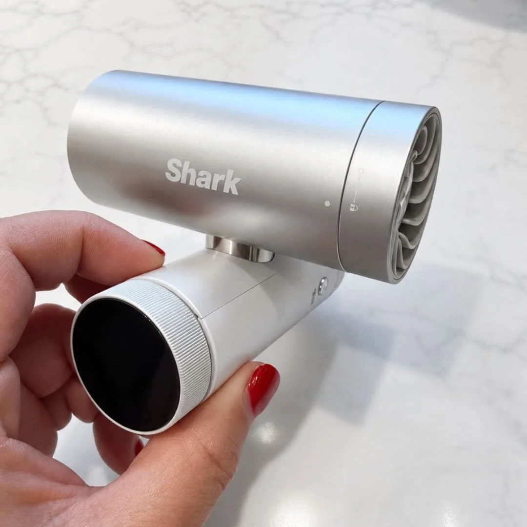 Hand holding a silver and white Shark personal cooling device with a compact cylindrical design against a marble background