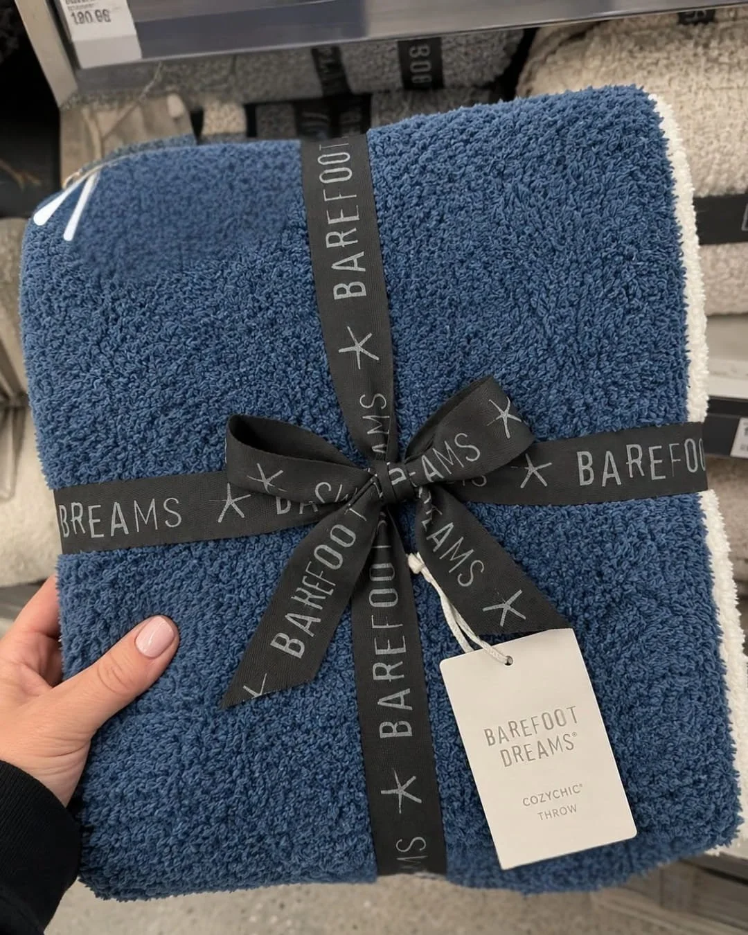 Folded Barefoot Dreams CozyChic throw blanket in slate blue with branded black ribbon and hang tag in a store