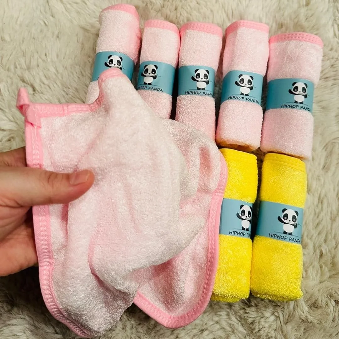 Set of HIPHOP PANDA baby washcloths, including five pink and two yellow towels with blue panda-branded bands, displayed on a cream shaggy rug with one unfolded pink towel held by a hand.