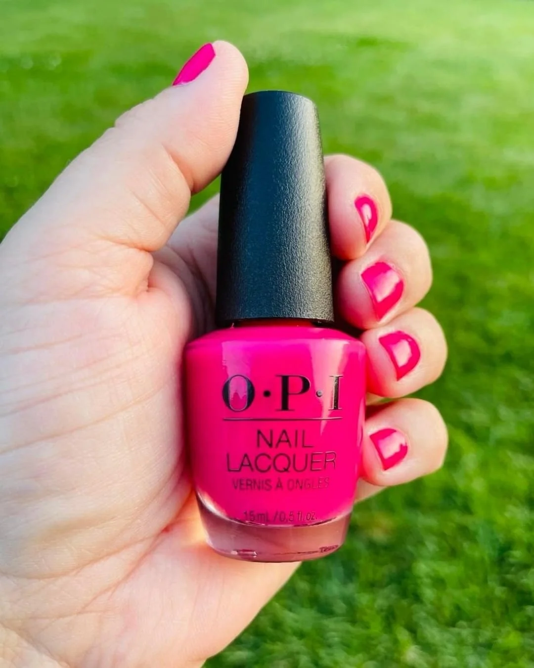 OPI hot pink nail polish bottle held in hand with matching painted nails outdoors