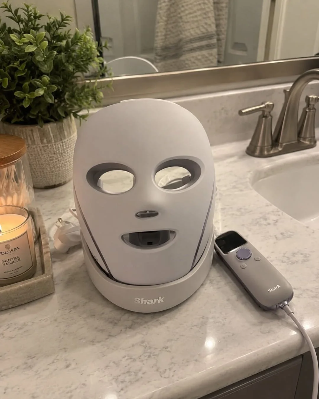 Shark LED face mask in charging base with handheld remote on a marble bathroom countertop