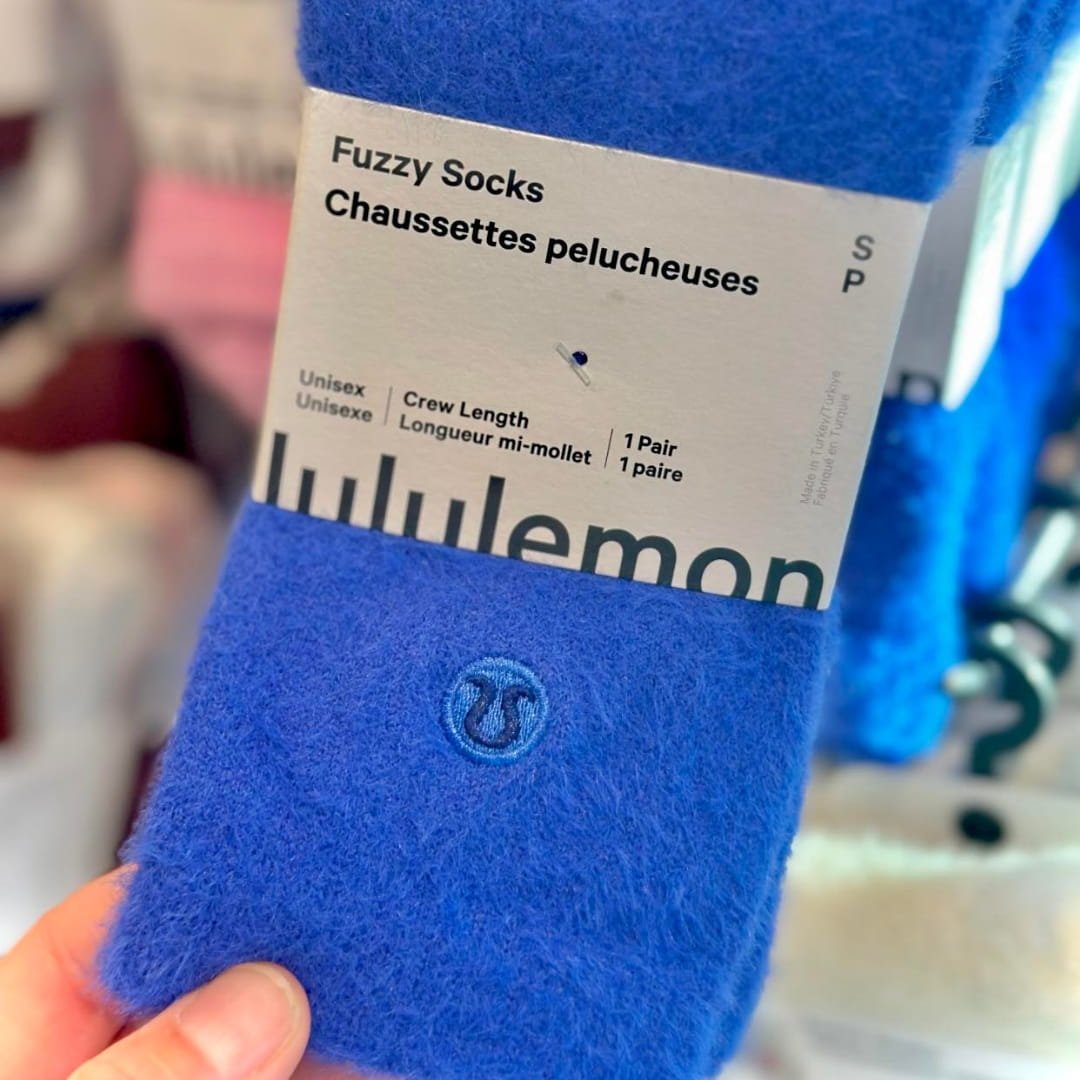Lululemon fuzzy socks in royal blue with a soft texture, packaged with a bilingual label in English and French, highlighting unisex crew length and size small, held in a retail setting.