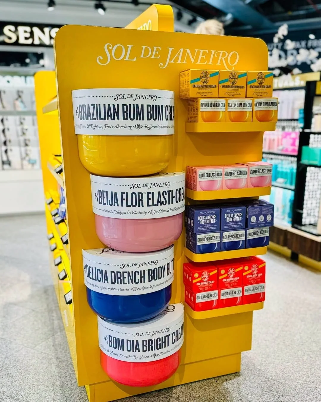 Retail display of Sol de Janeiro body cream set featuring colorful body creams and matching product shelves in a store