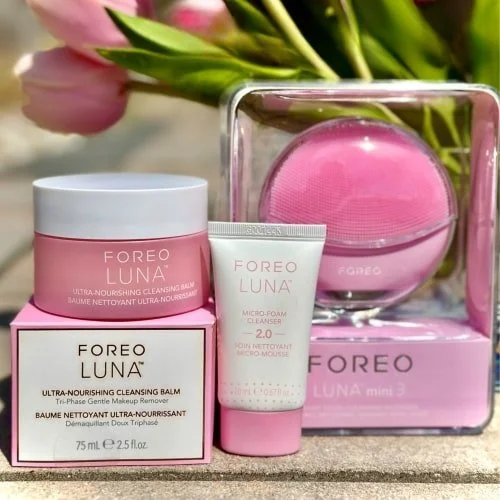 FOREO LUNA skincare set featuring a pink cleansing balm, micro-foam cleanser, and LUNA mini 3 facial device, displayed against a soft-focus background of pink tulips.
