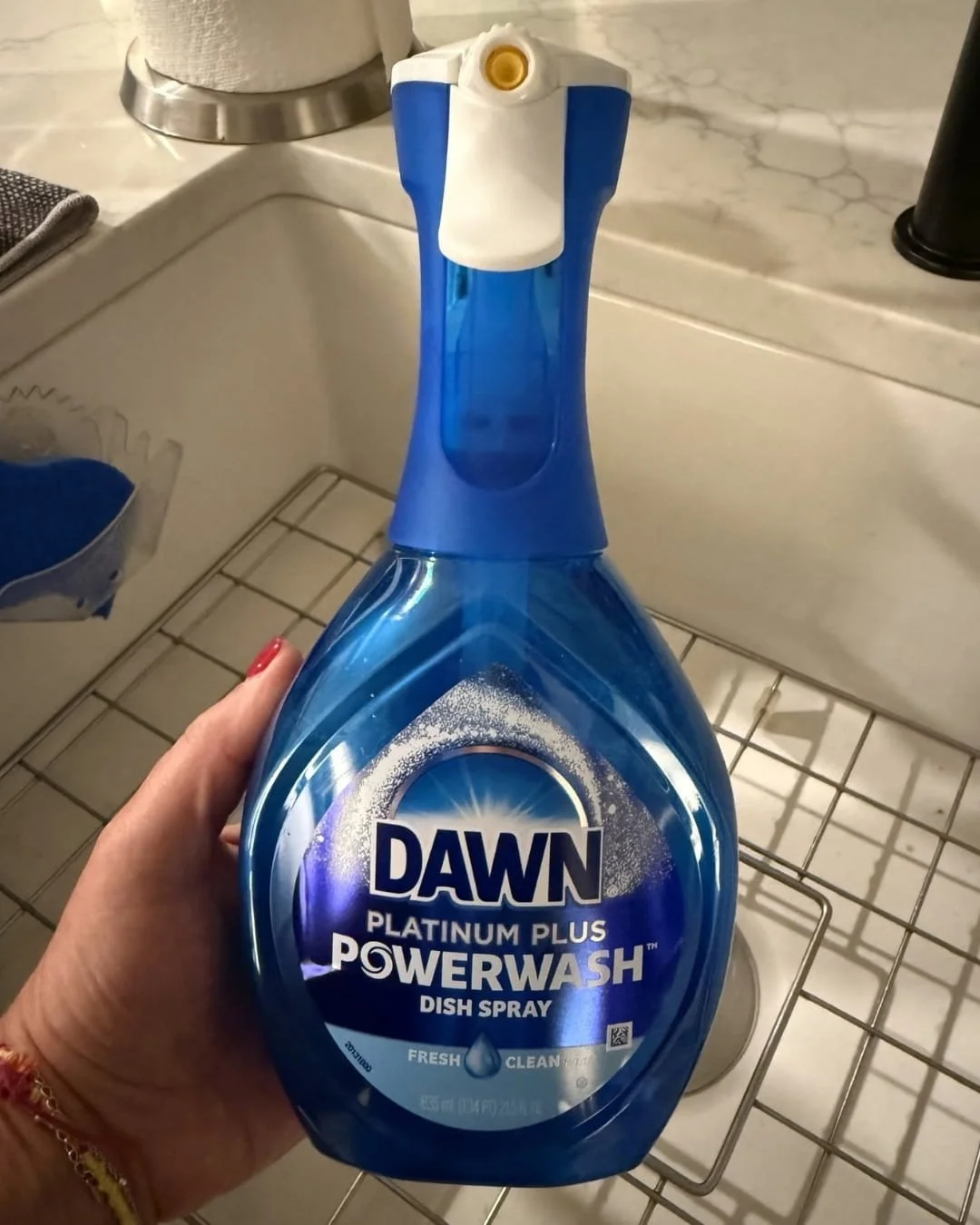 Hand holding Dawn Platinum Plus Powerwash dish spray bottle over a white kitchen sink