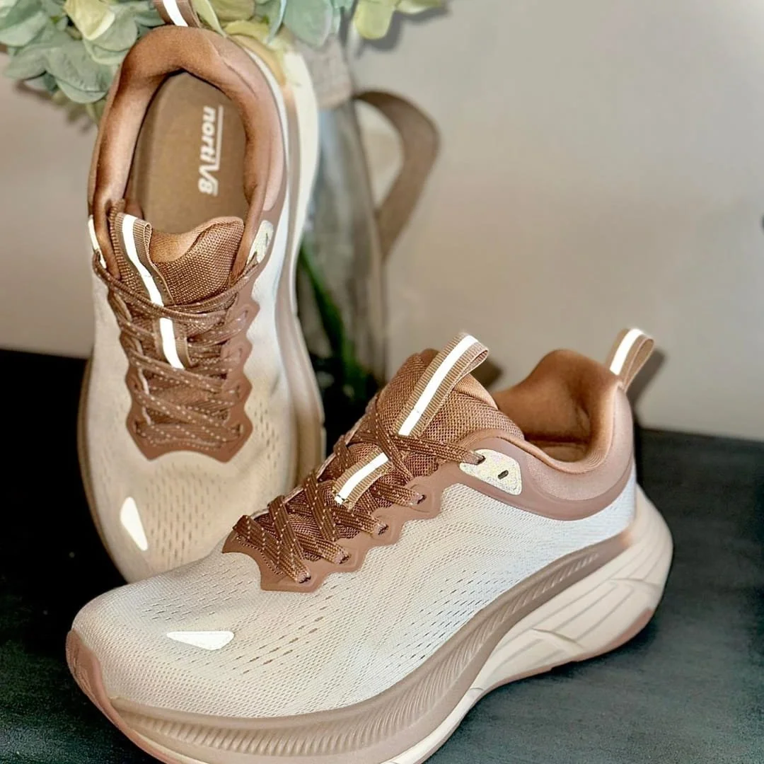 NORTIV8 running shoes in beige with a mesh upper, tan laces featuring reflective accents, sculpted midsoles, and pull-tabs, displayed on a dark textured surface with a soft-focus background.