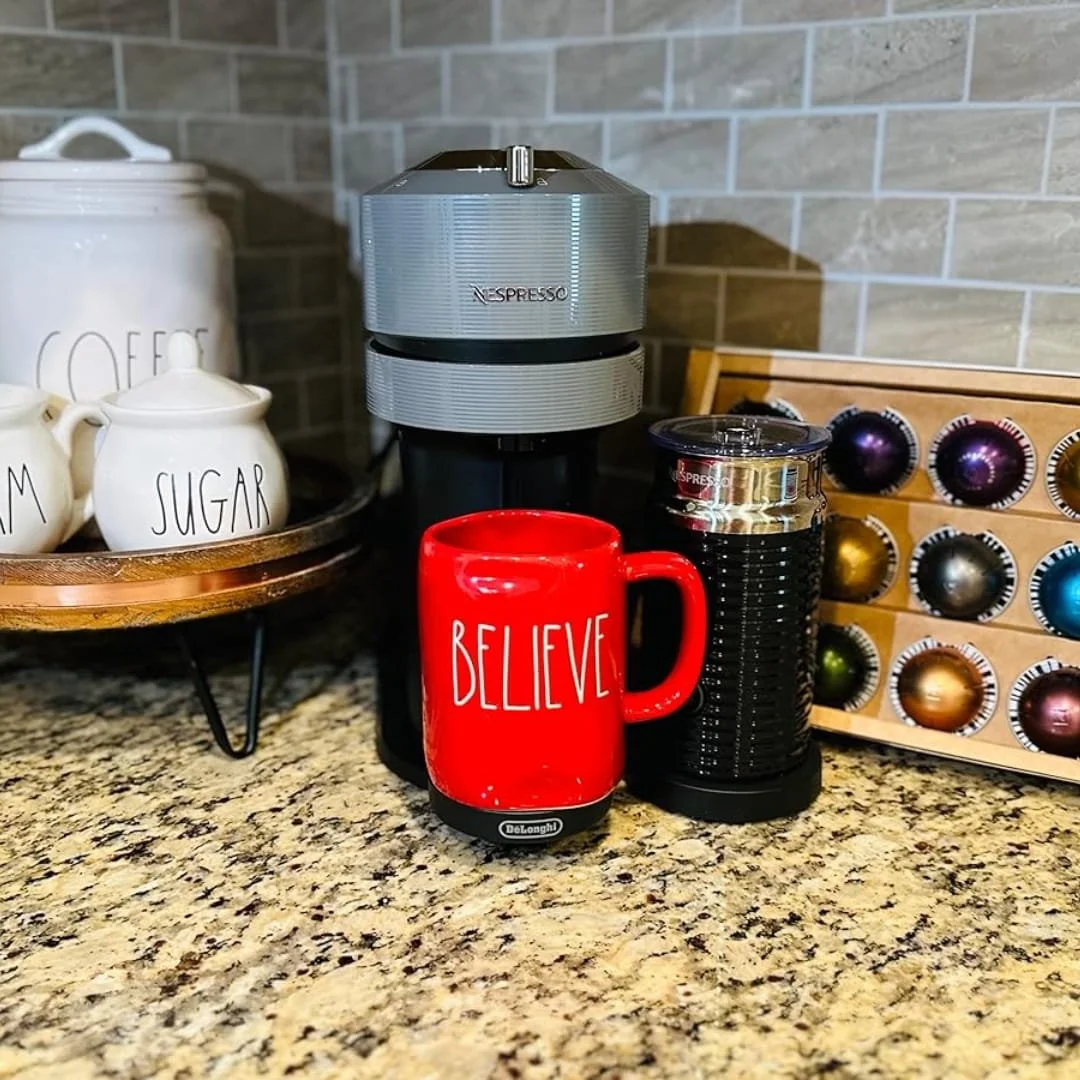 Nespresso Vertuo Next coffee maker with a red 'BELIEVE' mug, milk frother, and coffee capsules on a granite countertop.