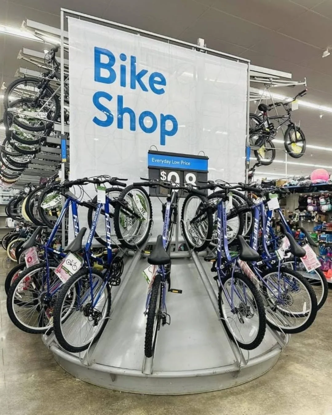 Display of kids bikes in a retail bike shop featuring multiple blue Huffy mountain bikes arranged on a circular rack under a Bike Shop sign