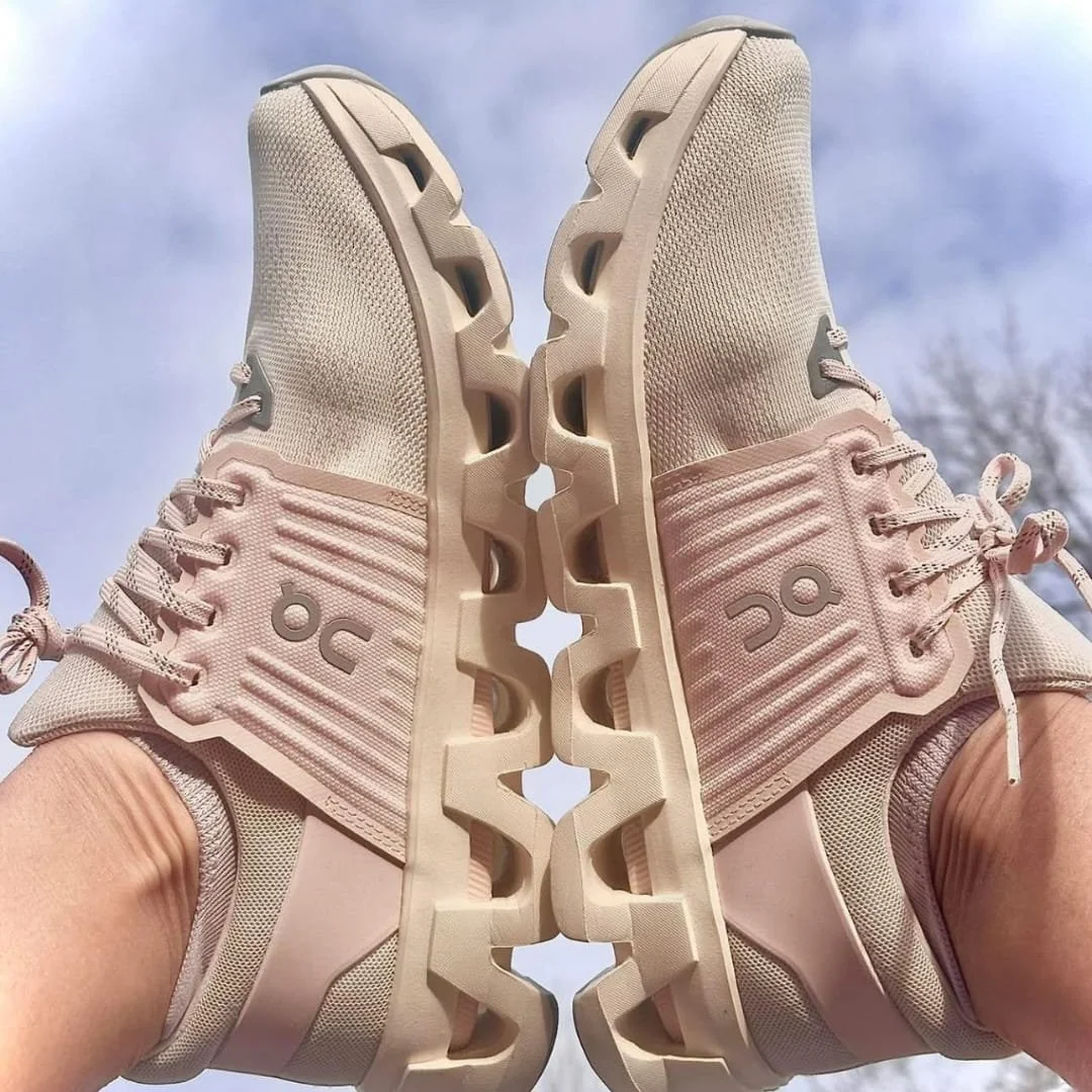 On Cloudswift running shoes in light pink with breathable mesh upper, ribbed side panels, and signature cloud-cushioned soles, displayed against a blurred outdoor background with sky and trees.