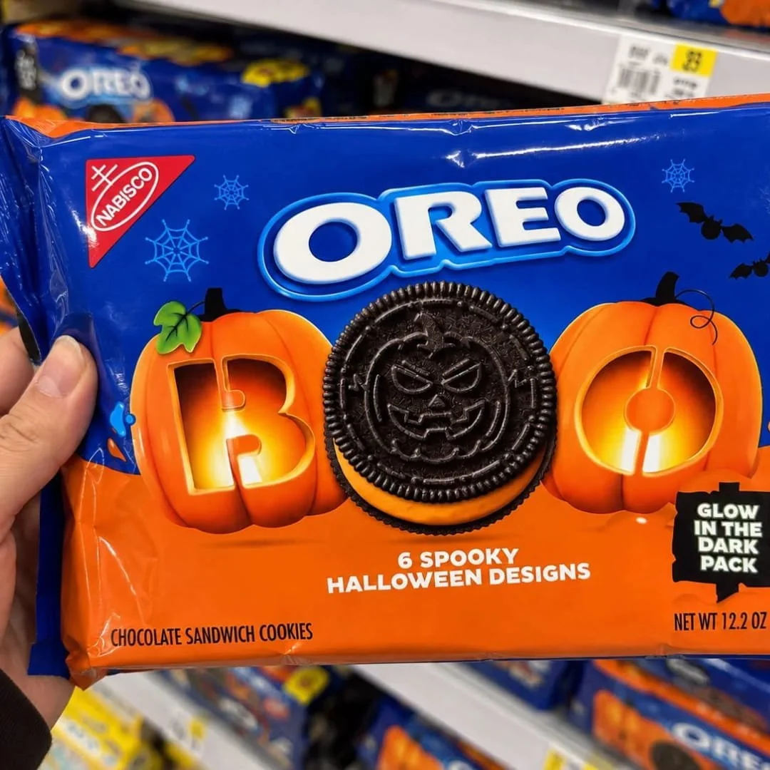 Hand holding OREO Halloween chocolate sandwich cookies package with orange cream, spooky cookie designs, and glow-in-the-dark packaging