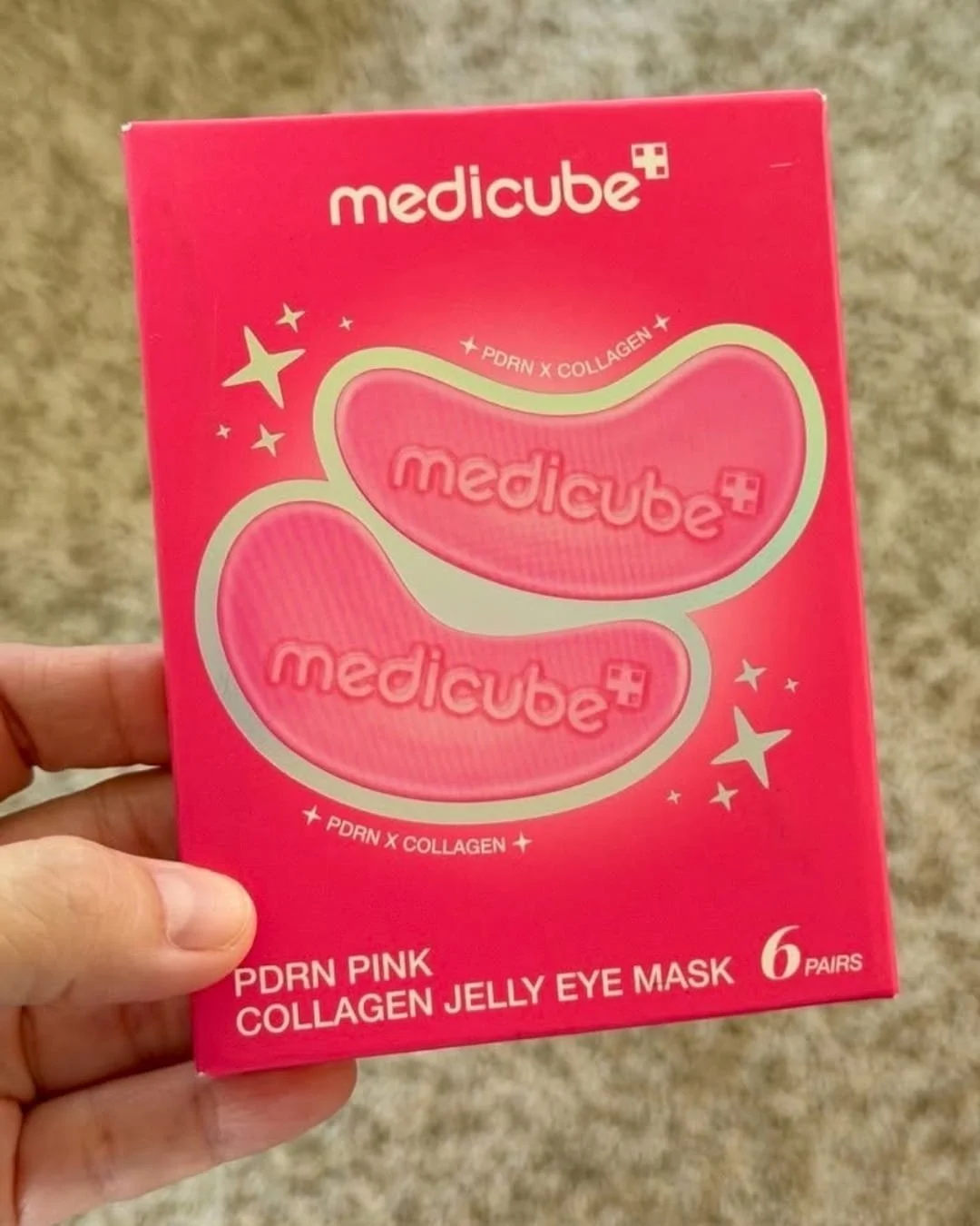 Hand holding Medicube PDRN Pink Collagen Jelly Eye Mask box with bright pink packaging and under-eye patch design