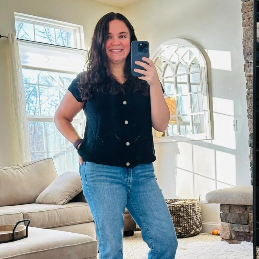 Nicole, a lifestyle blogger, smiling while taking a mirror selfie in a cozy, well-lit living room with stylish decor and natural sunlight streaming through a large window.