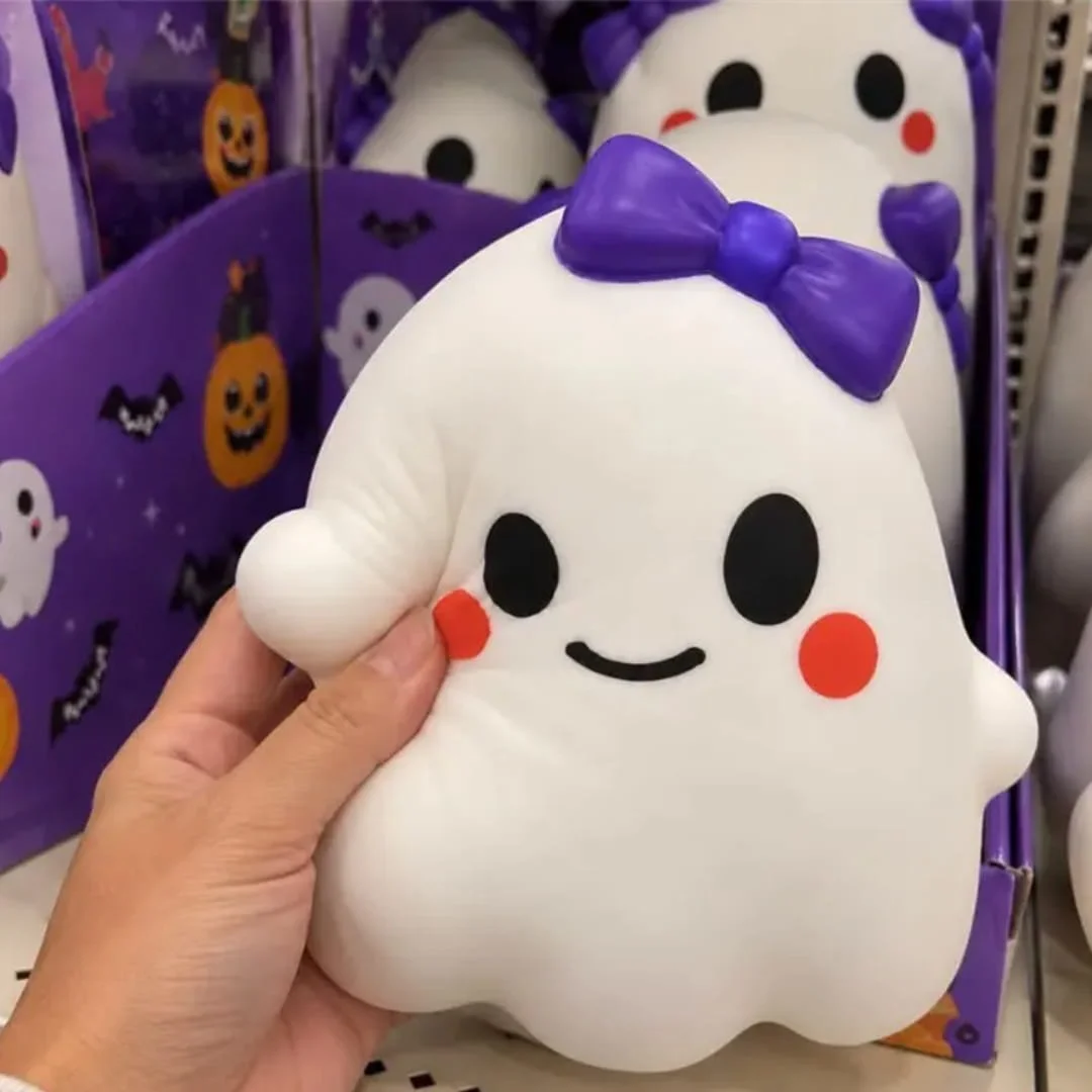 Hand holding a white ghost squishy squeeze toy with a purple bow in a Halloween retail display